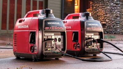 Two Honda generators sit side by side on the terrace of a nice residential home.  