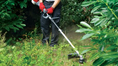 A person uses a Honda handheld on overgrown weeds and brush.  