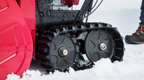 Closeup of the track wheels on a snowblower driving on snow.  